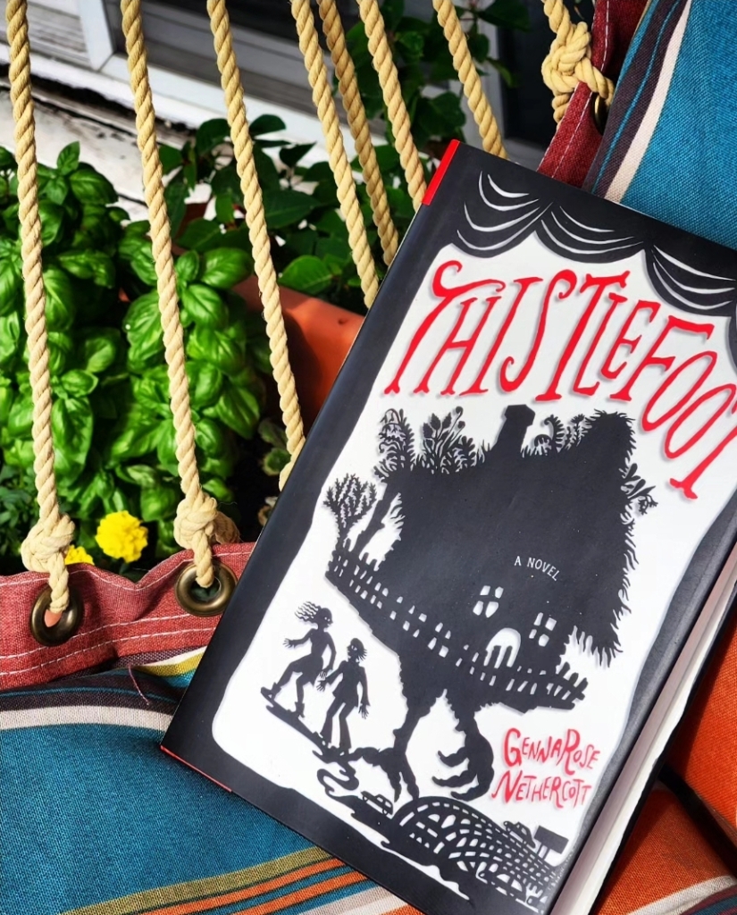 The book Thistlefoot by GennaRose Nethercott on a multicolored chair swing next to yellow marigolds and basil plants.